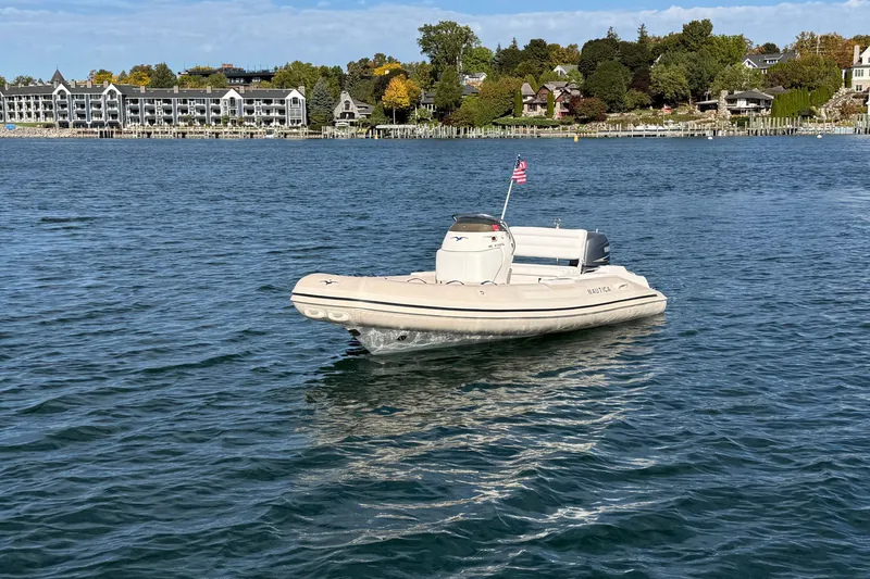 Slide: The Image of 2004 Nautica RIB 15 Widebody boat on water with scenic shoreline background. - 2