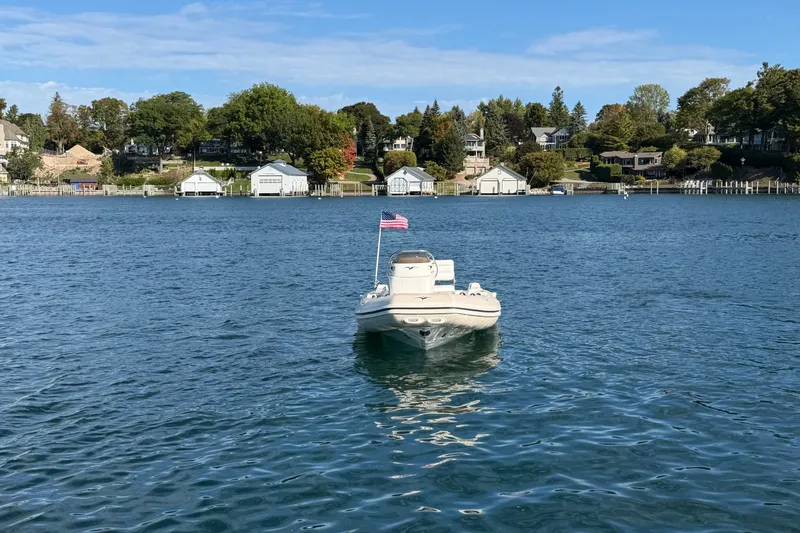 Slide: The Image of 2004 Nautica RIB 15 WIDEBODY boat on a serene lake with shoreline houses. - 14