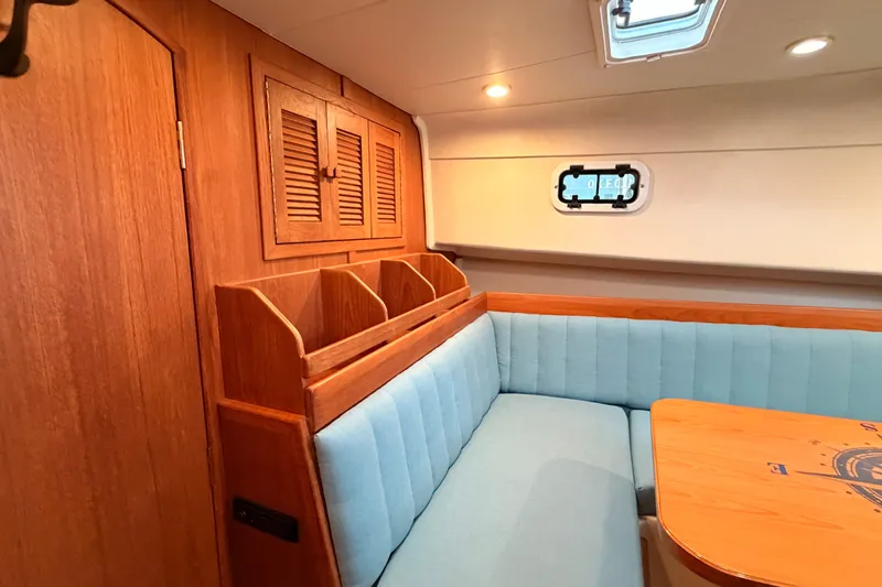 Slide: The Image of 2001 Mainship Pilot 34 interior with wood cabinetry, blue seating, and a small window. - 33