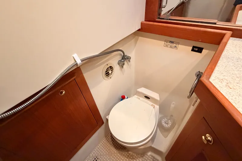 Slide: The Image of 2001 Mainship Pilot 34 boat bathroom with toilet, wooden cabinetry, and shower hose. - 29
