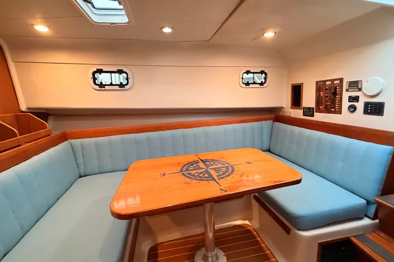 Slide: The Image of Interior of 2001 Mainship Pilot 34 with blue seating and compass-themed wooden table. - 34