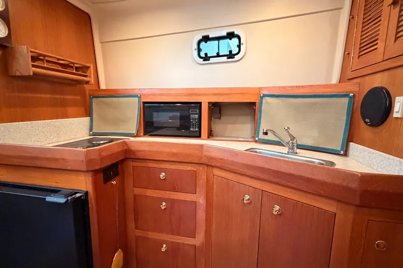 Slide: The Image of 2001 Mainship Pilot 34 boat kitchen with wood cabinetry, sink, stove, and microwave. - 27