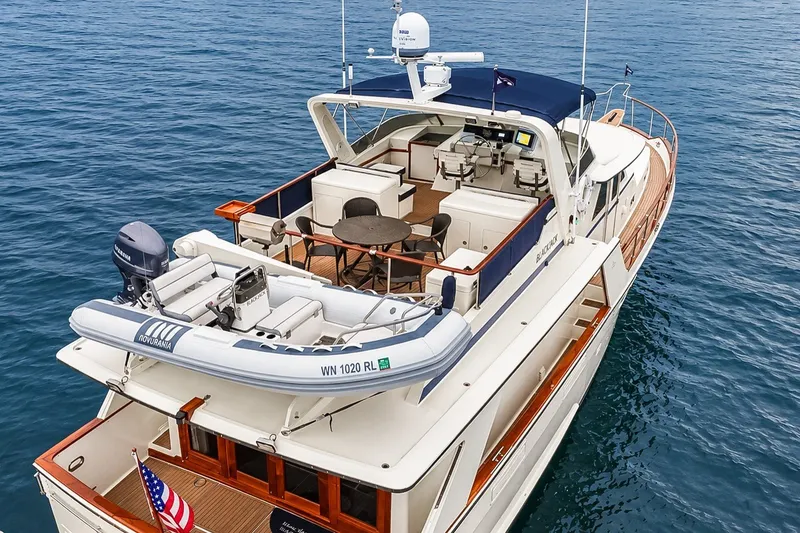 Slide: The Image of 1991 Tollycraft 61 Pilothouse Motor Yacht on calm blue water, featuring spacious deck and tender. - 11