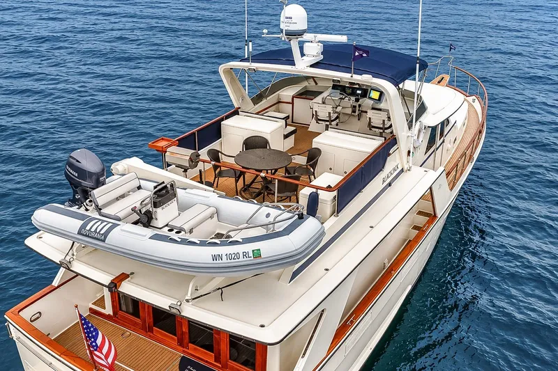 Slide: The Image of 1991 Tollycraft 61 Pilothouse Motor Yacht on open water, featuring a spacious deck and tender. - 62