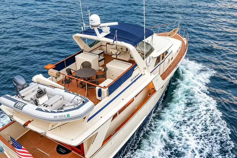 Slide: The Image of 1991 Tollycraft 61 Pilothouse Motor Yacht cruising on open water, featuring spacious deck and tender. - 7