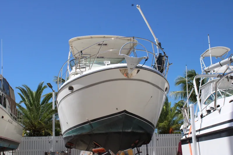 The Image of 1999 Maxum 4600 SCB yacht on dry dock, surrounded by palm trees and clear blue sky. - 0