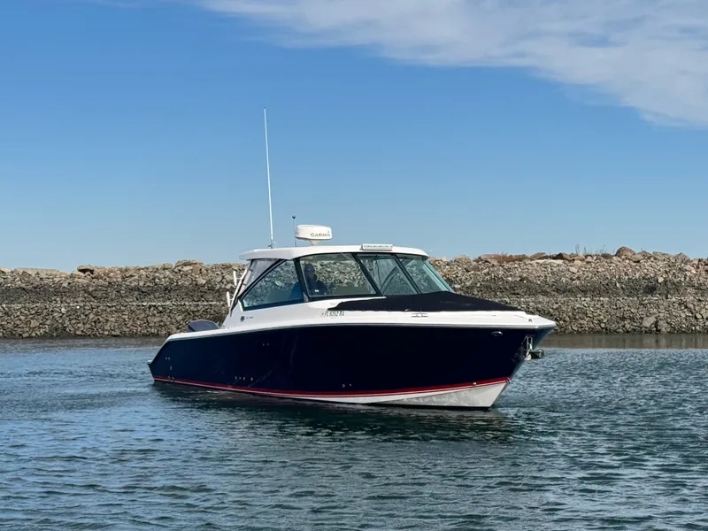 Slide: The Image of 2016 Pursuit DC 325 Dual Console on calm water near a rocky shoreline. - 3