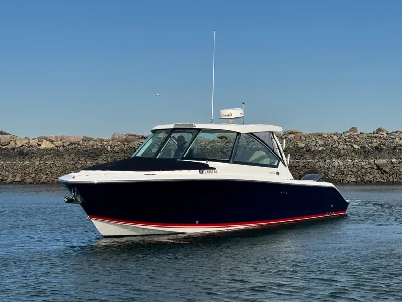 Slide: The Image of 2016 Pursuit DC 325 Dual Console on calm water near a rocky shoreline. - 6