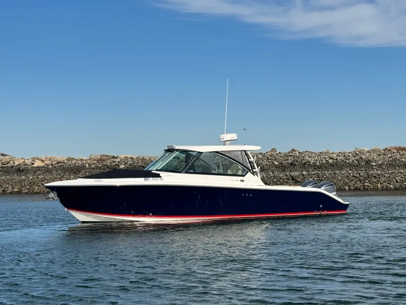 Slide: The Image of 2016 Pursuit DC 325 Dual Console on calm water near a rocky shoreline. - 8