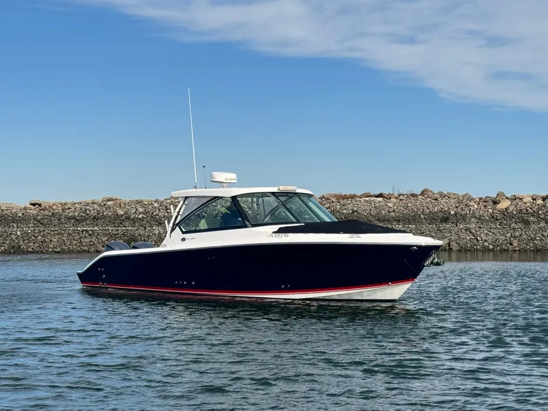 Slide: The Image of 2016 Pursuit DC 325 Dual Console on calm water near a rocky shoreline. - 2