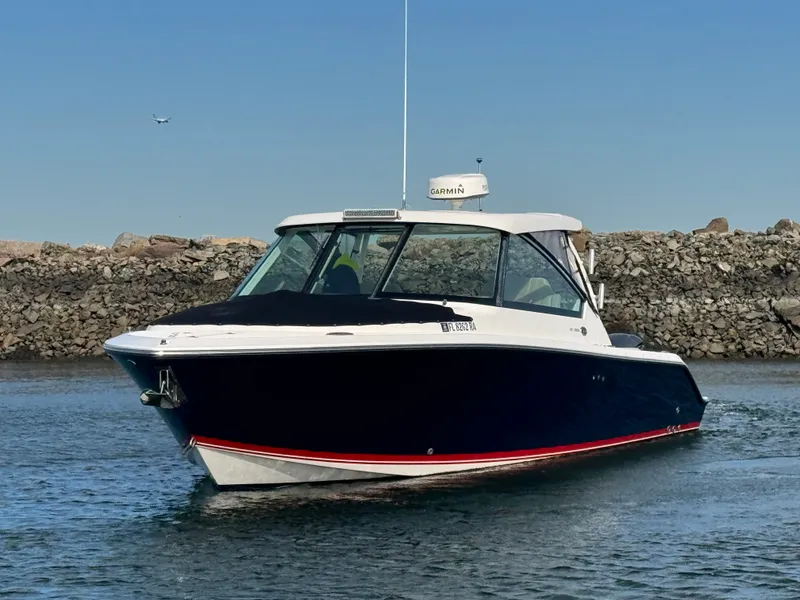 Slide: The Image of 2016 Pursuit DC 325 Dual Console on the water near a rocky shoreline. - 5