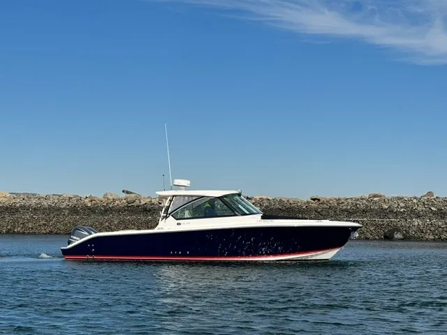 The Image of A 2016 Pursuit DC 325 Dual Console boat on calm water near a rocky shoreline. - 0