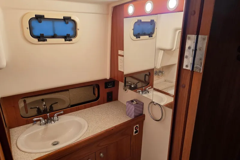 Slide: The Image of Bathroom interior of 2002 Mainship 430 Trawler with sink, mirror, and porthole window. - 17