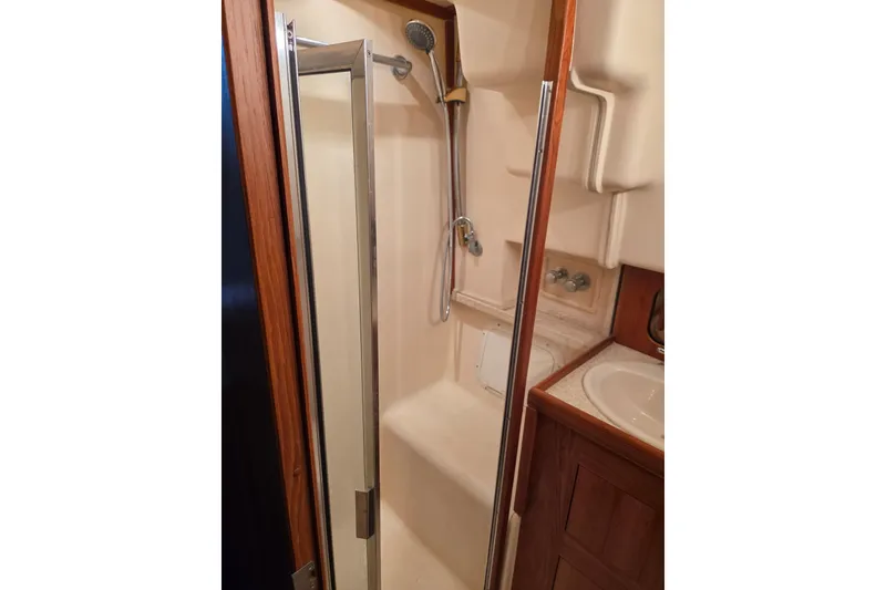 Slide: The Image of 2002 Mainship 430 Trawler bathroom with shower, sink, and wooden cabinetry. - 19