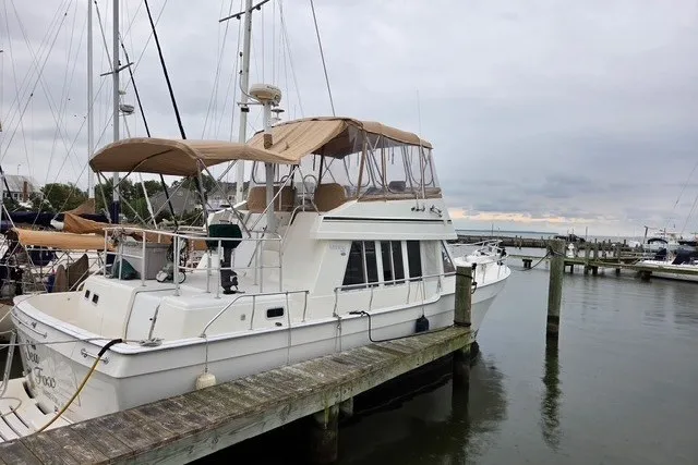 The Image of 2002 Mainship 430 Trawler docked at a marina, featuring a beige canopy. - 0