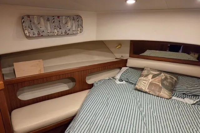 Slide: The Image of 2002 Mainship 430 Trawler cabin interior with striped bedding and wooden accents. - 12