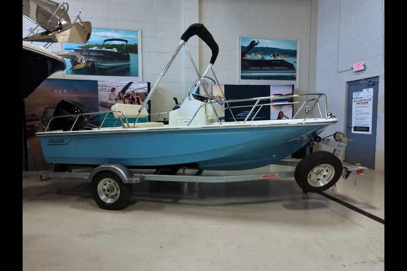 Slide: The Image of 2027 Boston Whaler 150 Montauk boat displayed indoors on a trailer. - 1