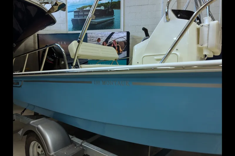 Slide: The Image of 2027 Boston Whaler 150 Montauk boat in showroom, side view with trailer. - 2