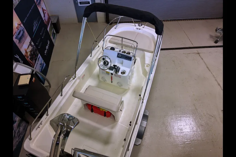 Slide: The Image of 2027 Boston Whaler 150 Montauk boat with steering console and seating, displayed indoors. - 4