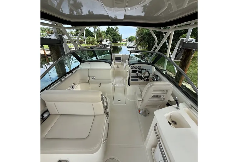 Slide: The Image of 2019 Boston Whaler 270 Vantage boat interior with seating and helm, docked by lush greenery. - 22