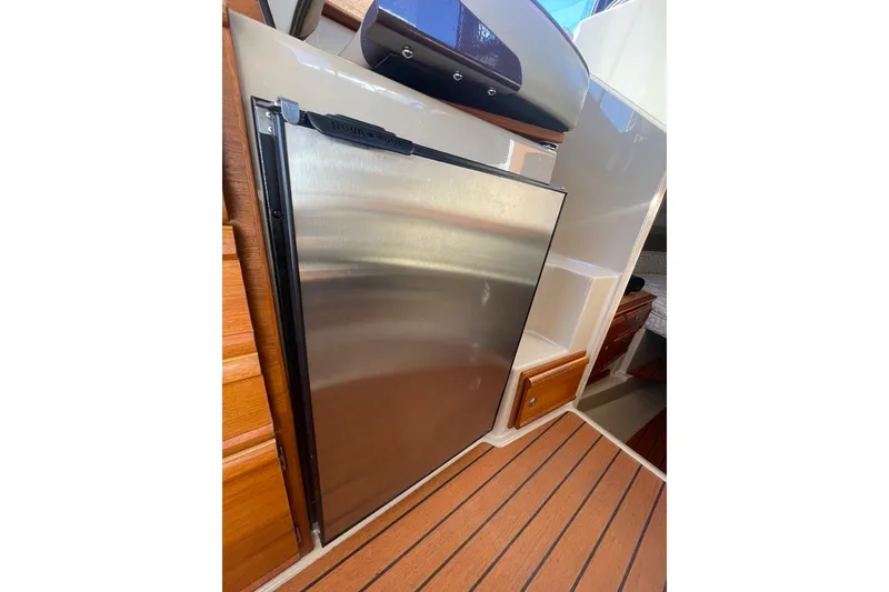 Slide: The Image of 2018 Ranger Tug R-27 interior with stainless steel refrigerator and wooden cabinetry. - 16