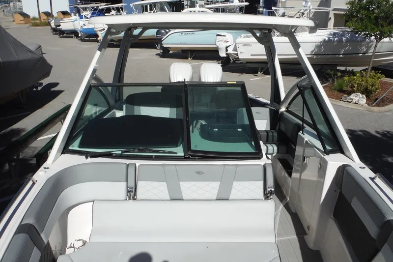 Slide: The Image of 2025 Chaparral 310 OSX boat interior with seating and windshield in a marina setting. - 43