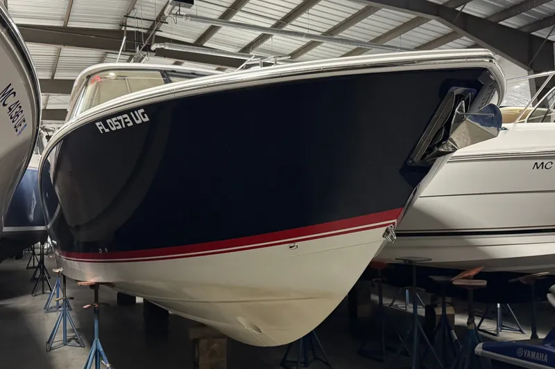 Slide: The Image of 2026 Pursuit DC 326 Dual Console boat in storage, blue hull with red stripe. - 2