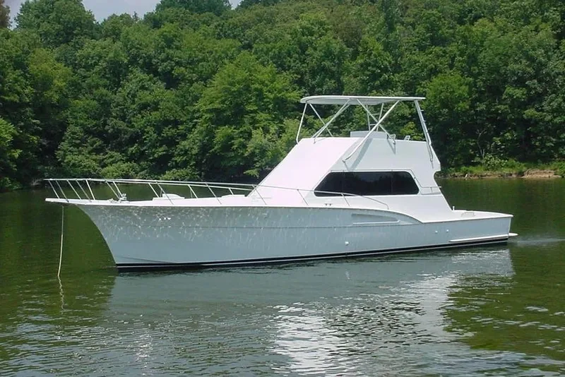 Slide: The Image of A white 1976 Hatteras 53 Convertible floats on a calm river, surrounded by trees. - 2
