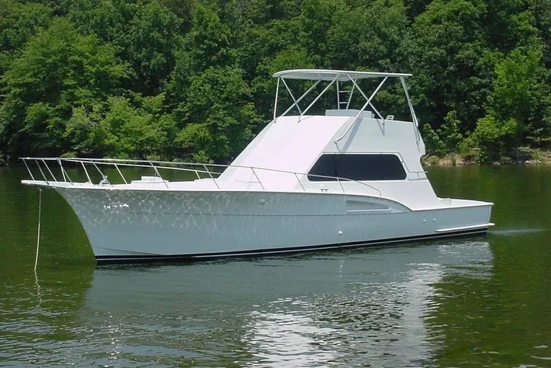 Slide: The Image of A white 1976 Hatteras 53 Convertible boat on calm water, surrounded by trees. - 3