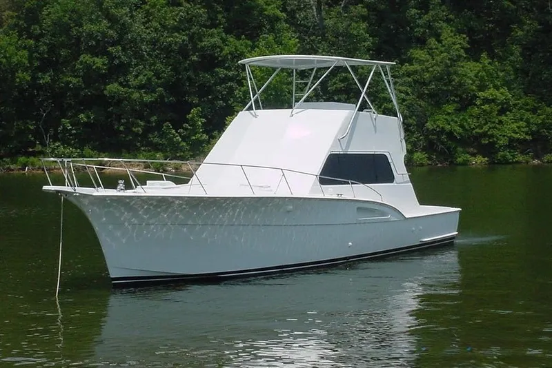 The Image of A white 1976 Hatteras 53 Convertible boat on calm water, surrounded by trees. - 0