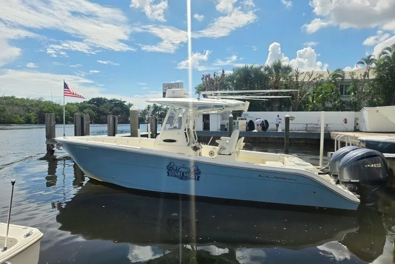 Slide: The Image of 2022 Cobia 280 Center Console boat docked by a waterfront with American flag. - 2
