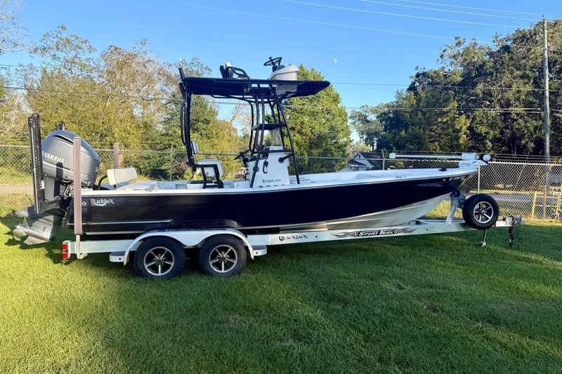 Slide: The Image of 2012 BlackJack 224 boat on trailer, parked on grass with trees in background. - 1