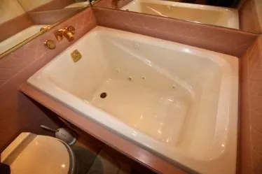 Slide: The Image of Large white bathtub with gold fixtures, pink tile surround, and adjacent toilet, custom 1989 design. - 32