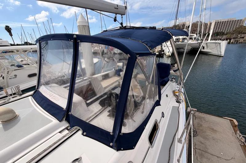 Slide: The Image of 2009 Hunter 33 sailboat docked, featuring blue canopy and clear panels, in a marina setting. - 20