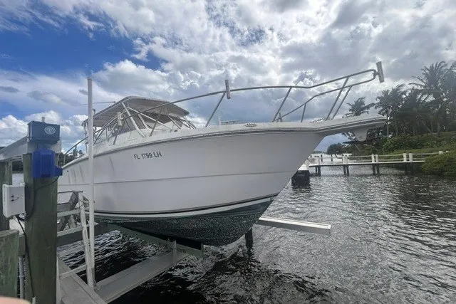 Slide: The Image of 2000 Shamrock 290 Walkaround boat docked by the water under a cloudy sky. - 14