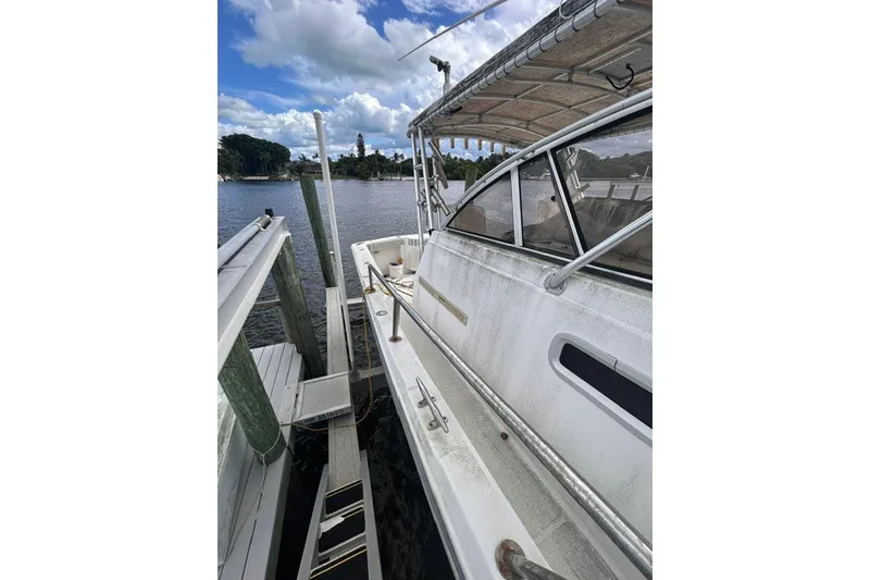 Slide: The Image of 2000 Shamrock 290 Walkaround boat docked by a scenic waterfront under a cloudy sky. - 11