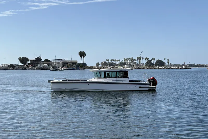 Slide: The Image of A 2021 Axopar 28 Cabin boat cruising on calm water with a shoreline in the background. - 2