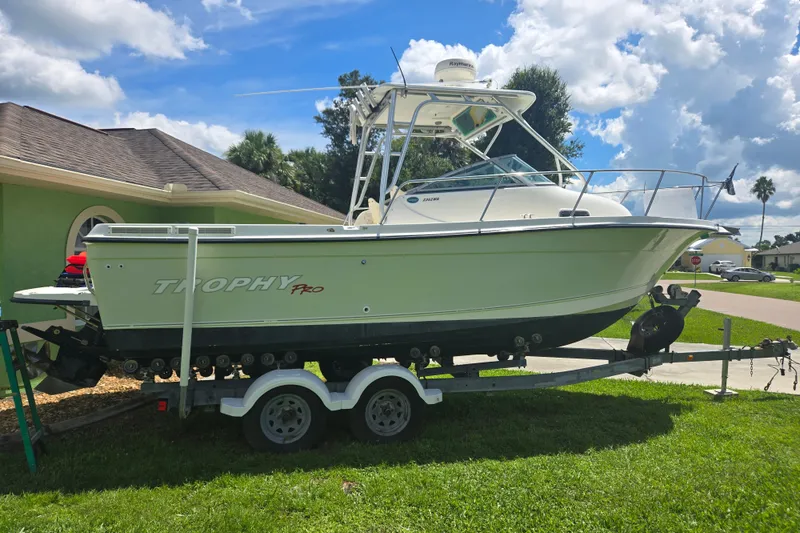 The Image of 2005 Trophy 2352 Walkaround boat on trailer, parked on grass under a partly cloudy sky. - 0