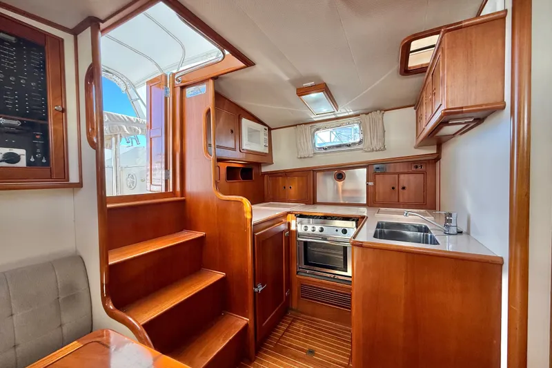 Slide: The Image of 1999 Grand Banks 38 Eastbay EX interior with wooden cabinetry, stairs, and kitchen area. - 19