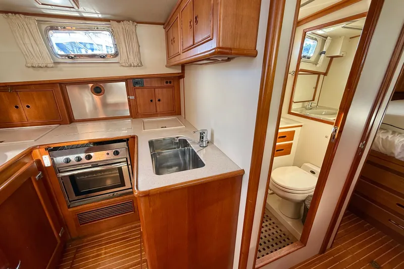 Slide: The Image of 1999 Grand Banks 38 Eastbay EX interior with kitchen and bathroom, featuring wood cabinetry and modern appliances. - 29