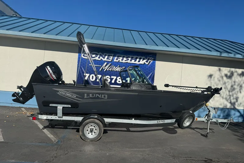 The Image of 2027 Lund 1650 Angler Sport boat on trailer, parked outside a marine shop. - 2