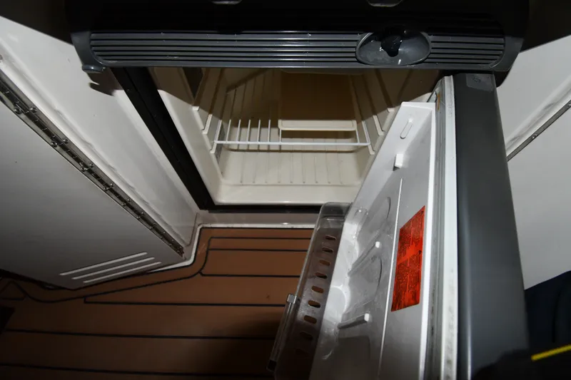 Slide: The Image of Open refrigerator inside 2005 Sea Ray 420 Sundancer yacht, showing empty shelves and wooden flooring. - 17