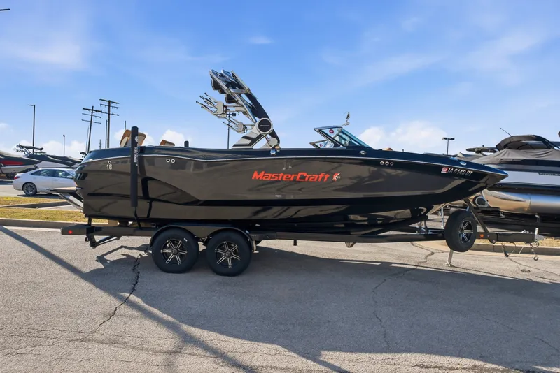 The Image of 2020 MasterCraft X24 boat on trailer, parked outdoors under clear blue sky. - 0
