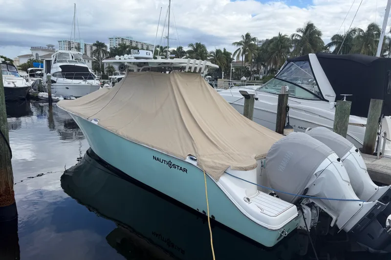 Slide: The Image of 2022 NauticStar 28 XS boat docked with cover, twin engines, marina background. - 60