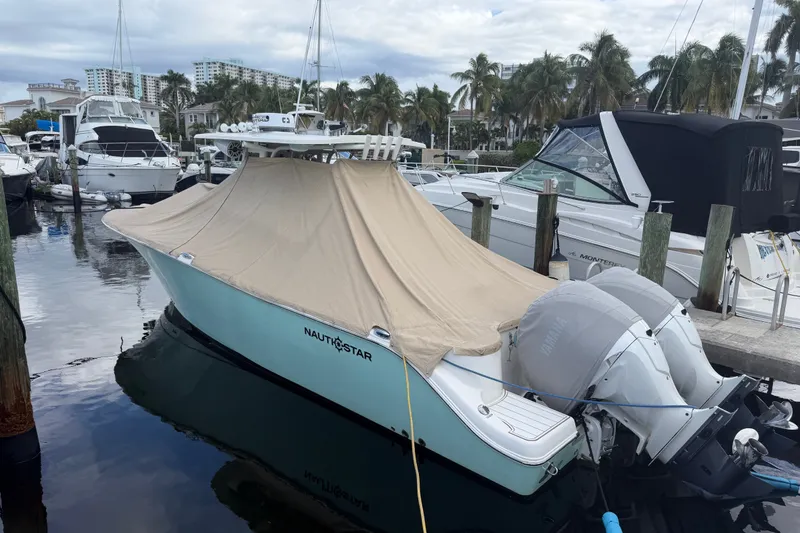 Slide: The Image of 2022 NauticStar 28 XS boat docked, covered with a beige tarp, in a marina setting. - 62