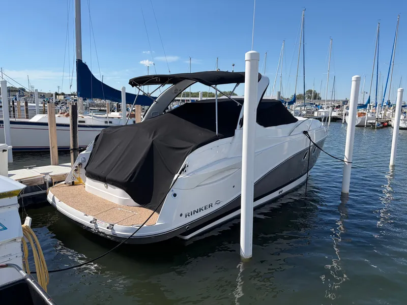 Slide: The Image of A 2013 Rinker 310 Express docked in a marina. It features a black cover and white hull. - 2