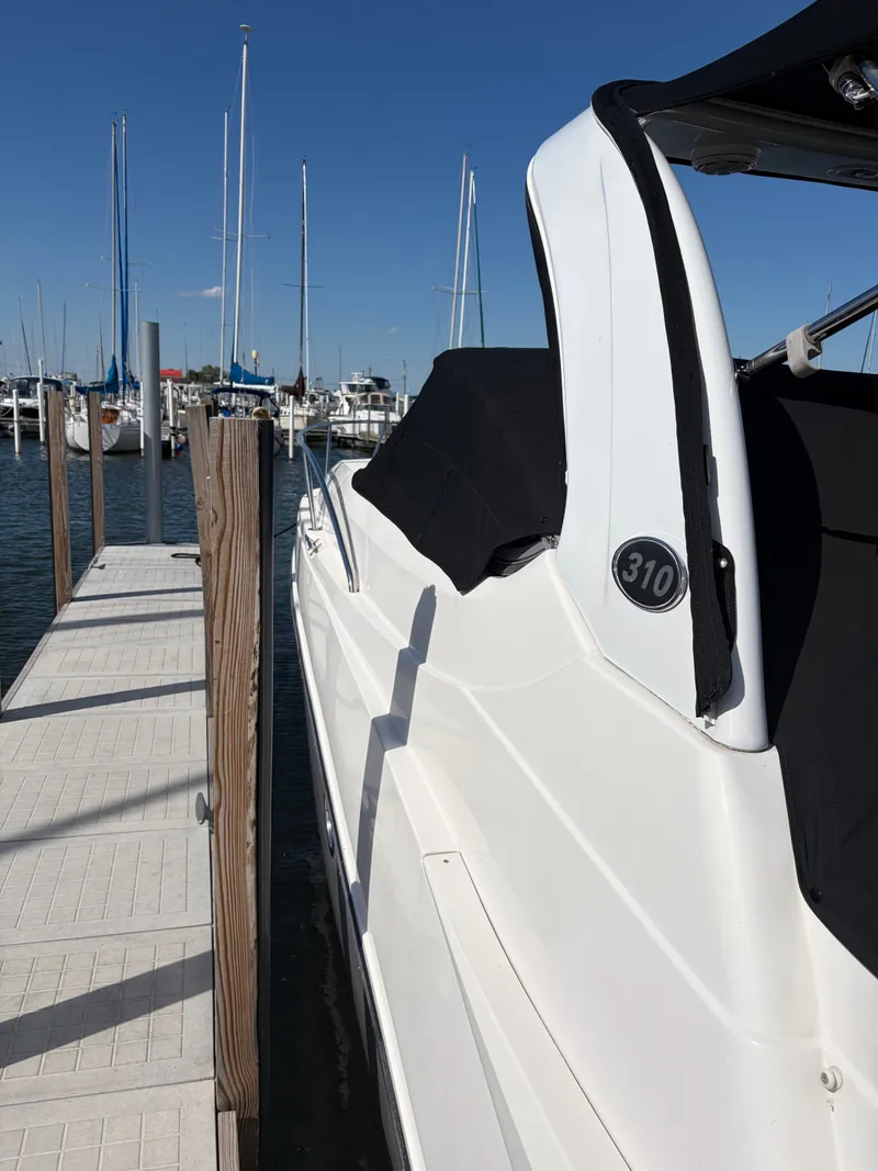 Slide: The Image of A 2013 Rinker 310 Express docked, featuring a sleek white hull and black canopy. - 3