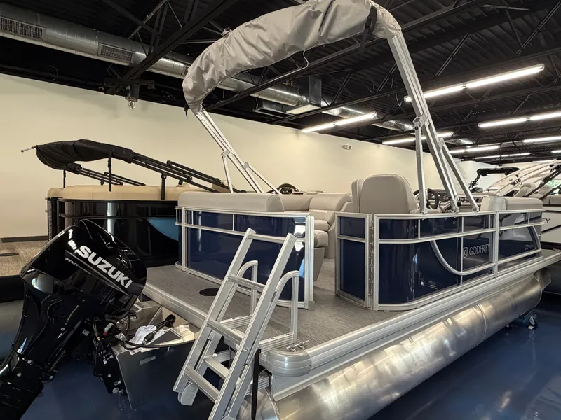 The Image of A modern pontoon boat with blue siding and a Suzuki outboard motor, displayed in a showroom. - 0