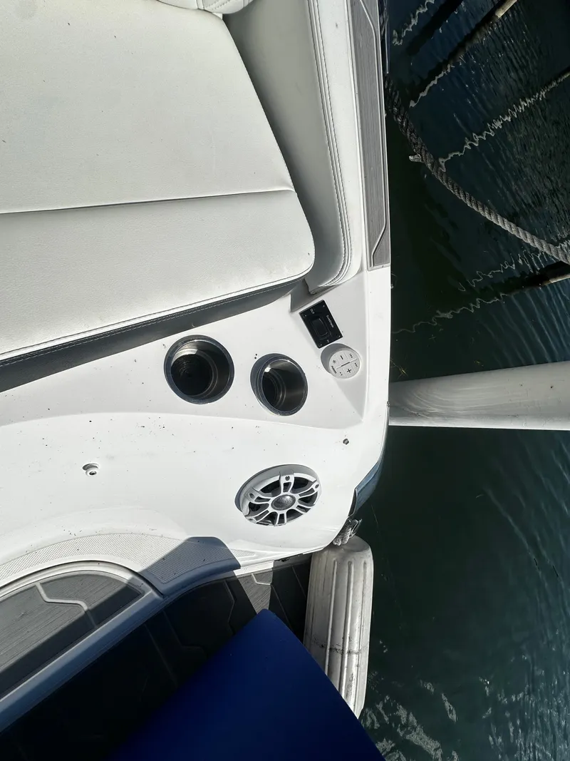 Slide: The Image of Part of a boat with white cushions, speaker, and cup holders by the water. - 14