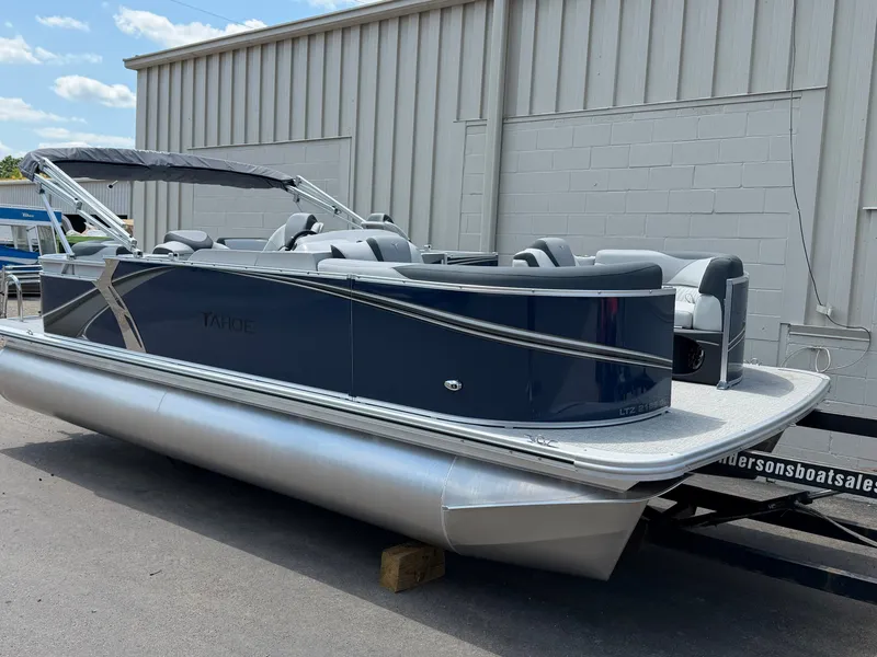 The Image of A modern pontoon boat with blue paneling and silver accents, parked in front of a building. - 0